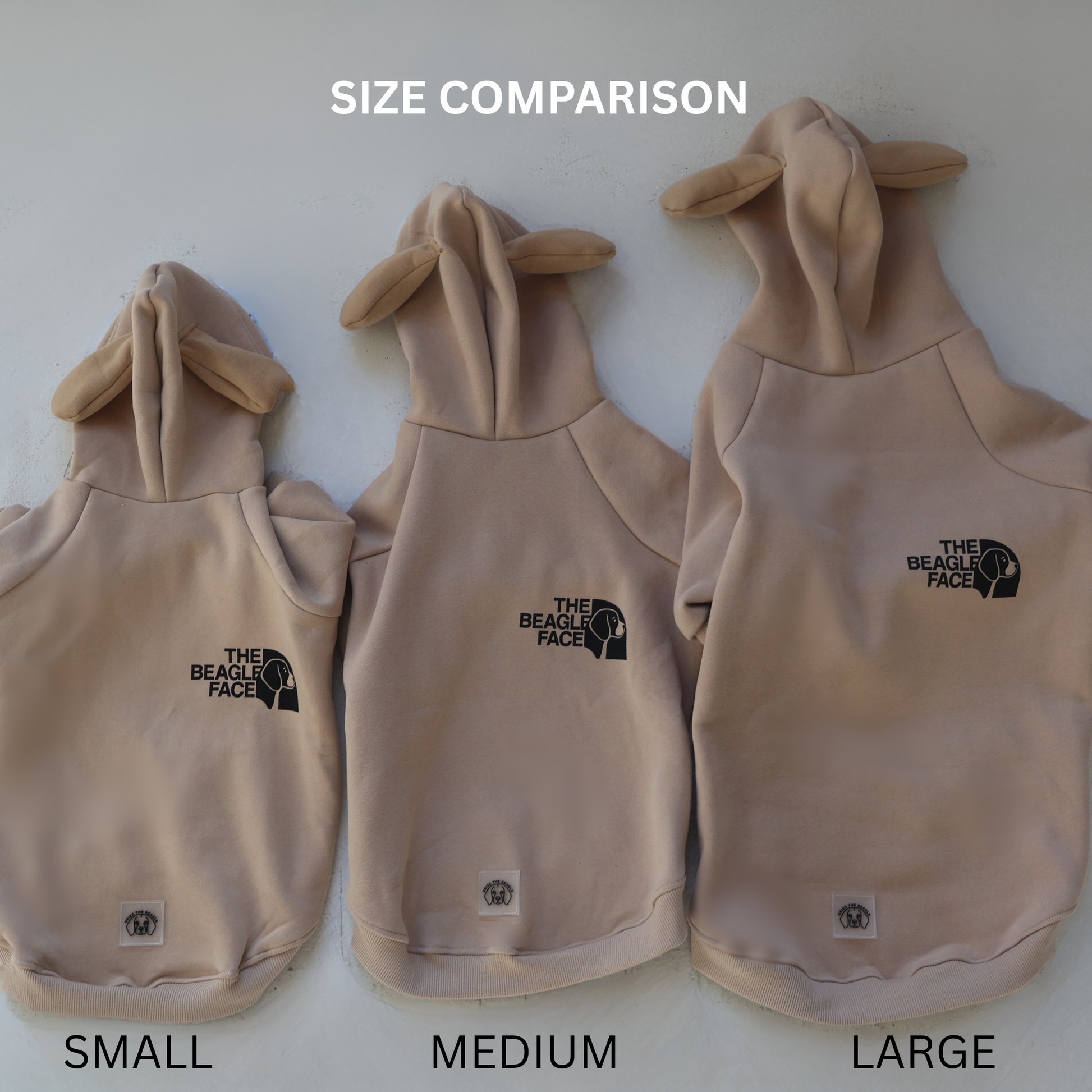 Three sizes of a beige dog hoodie with 'The Beagle Face' logo